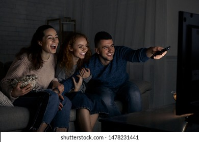 Excited Friends Watching TV And Switching Channels With Remote Controller At Home