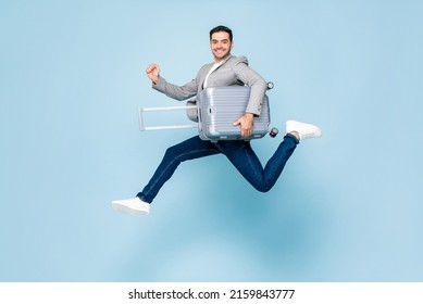 Excited Fun Caucasian Tourist Man With Baggage, Ready To Travel, Jumping In Studio Light Blue Color Isolated Background