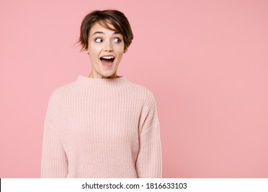 Excited Fun Happy Young Brunette Woman 20s Wearing Knitted Casual Sweater Keeping Mouth Open, Looking Aside Isolated On Pastel Pink Wall Background Studio Portrait. People Emotions Lifestyle Concept.