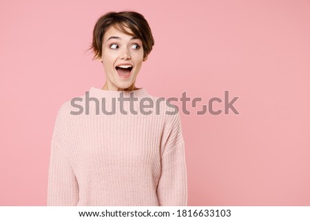 Excited fun happy young brunette woman 20s wearing knitted casual sweater keeping mouth open, looking aside isolated on pastel pink wall background studio portrait. People emotions lifestyle concept.