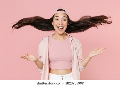 Excited fun young asian woman 20s in casual clothes cap posing isolated on pastel pink wall background studio. People lifestyle concept. Mock up copy space. Spreading hands throwing up fluttering hair