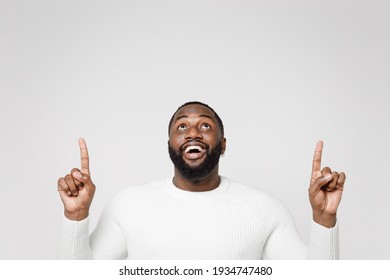 Excited funny cheerful young african american man 20s wearing casual basic sweater standing pointing index fingers up on mock up copy space isolated on white color wall background studio portrait