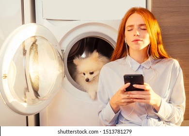 excited funny redhaired girl listening music with headphones,her adorable fluffy spitz inside the washing machine at home a pile of dirty clothes on the floor . - Powered by Shutterstock