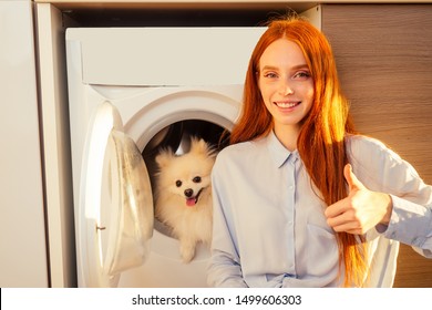 Excited Funny Redhaired Girl Sitting Next To Her Adorable Fluffy Spitz Inside The Washing Machine At Home . Spa Day For Pet Treatment Concept.