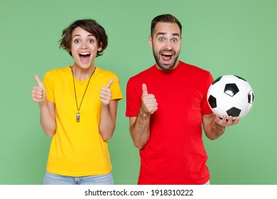 Excited Funny Young Couple Friends Sport Family Woman Man Football Fans In Yellow Red T-shirts Cheer Up Support Favorite Team With Soccer Ball Showing Thumbs Up Isolated On Green Background Studio