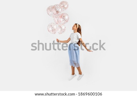 Excited funny young girl jumping high celebrating and holding colorful balloons isolated on white background. Birthday party