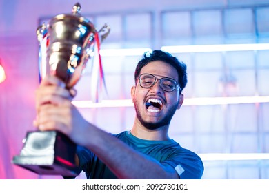 Excited gamer celebrating win by showing trophy to audience and shouting by looking at live streaming camera during esports tournament - concept of professional champion gamer
