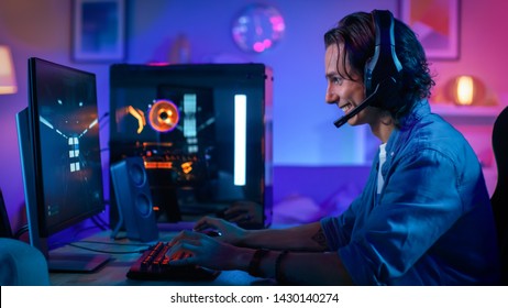 Excited Gamer Playing First-Person Shooter Online Video Game on His Personal Computer. Room and PC have Colorful Neon Led Lights. Young Man has Long Hair. Cozy Evening at Home. - Shutterstock ID 1430140274