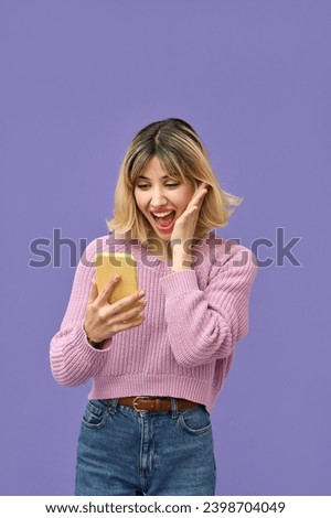 Excited gen z blonde young woman winner with smartphone, happy customer student girl looking amazed using mobile cell phone celebrating online prize win on purple background, vertical.