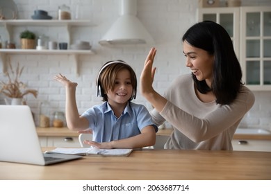 Excited Gen Z Schoolkid In Headphones Giving High Five To Happy Mom At Laptop. Mother Helping Son To Do School Home Work, Giving Praise And Support For Studying Achievement. Parenthood, Homeschooling