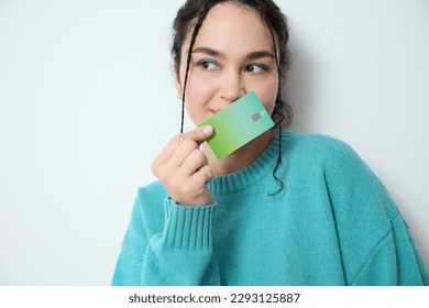 Excited gen z woman with vivid make-up green eye shadow holds a green credit card standing on white backdrop in studio smiles as she showcases her preference of electronic banking and online shopping. - Shutterstock ID 2293125887