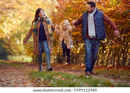 Excited Girl Being Swung By Parents On Family Autumn Walk Through Countryside