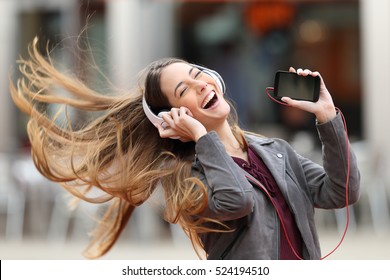 Excited girl dancing and listening music with headphones and smart phone in the street with hair moving - Powered by Shutterstock