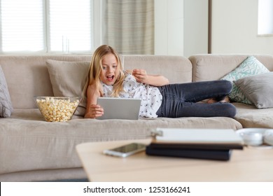 Excited girl lying down on sofa at home and watching a digital tablet.  - Shutterstock ID 1253166241