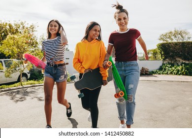 Excited girls walking in the street with their longboard and skateboards. Smiling teenage girls getting ready to skate on the street on a sunny day. - Powered by Shutterstock