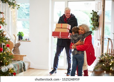 Excited Grandson Greeting Grandparents With Presents Visiting On Christmas Day