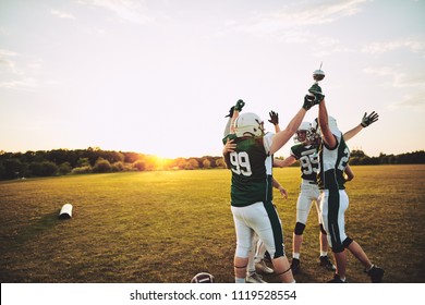 Excited group of American football players standing together in a huddle and raising a championship trophy in celebration - Powered by Shutterstock