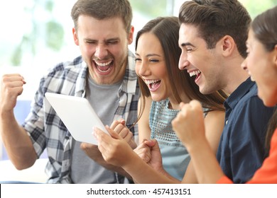 Excited group of four friends viewing media content on line from a tablet in a house interior