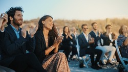 Excited Guests Sitting In An Outdoors Venue And Clapping Hands. Multiethnic Beautiful Diverse Crowd Celebrating An Event, Wedding Or Concert. Inspiring Day With Beautiful Warm Weather.