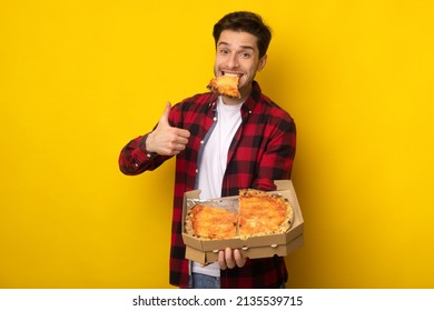 Excited Guy Holding Pizza Box Eating Slice And Gesturing Thumbs Up Smiling To Camera Posing With Snack In Mouth On Yellow Studio Background Wall. Young Man Approving Fastfood Taste. I Like Junk Food