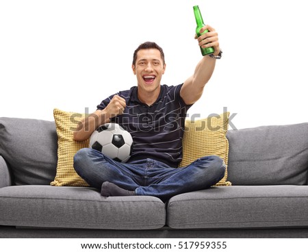 Excited guy sitting on a couch having a beer and watching football isolated on white background 