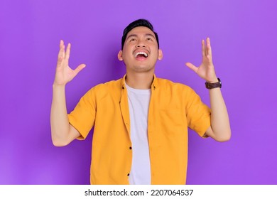 Excited Handsome Young Asian Man Looking Up With A Happy Expression While Raising Arms Isolated On Purple Background