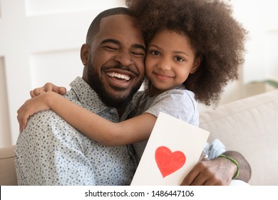 Excited happy african american dad holding cute little daughter and greeting card with red heart, tender Fathers Day celebration concept. Black preschool smiling girl hugging daddy, looking at camera. - Shutterstock ID 1486447106