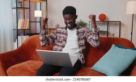 Excited Happy African American Teen Guy Use Laptop Pc Typing Browsing Say Wow Yes Found Out Great Big Win News Doing Winner Gesture. Young Man Working On Computer At Home Office In Living Room On Sofa