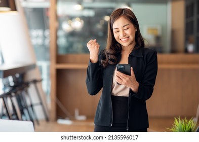 Excited Happy Asian Woman Looking At The Phone Screen, Celebrating An Online Win, Overjoyed Young Asian Female Screaming With Joy, Isolated Over A White Blur Background