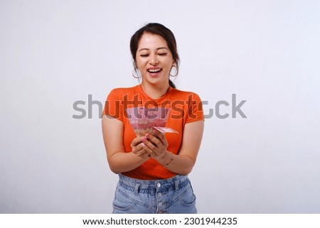 Excited and happy Asian woman wearing casual shirt holding Indonesian money isolated on white background