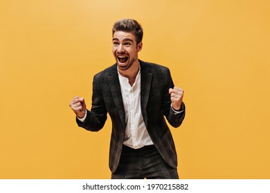 Excited Happy Bearded And Rejoices On Orange Background. Emotional Young Guy In Checkered Suit And White Shirt Laughs On Isolated.