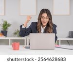 Excited happy business woman, young caucasian 20s excited happy business woman sitting office desk using laptop doing winner success gesture. Celebrating clenched fist up. Wear formal jacket.