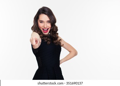 Excited happy confident curly retro styled young woman in black dress pointing at camera isolated over white background
