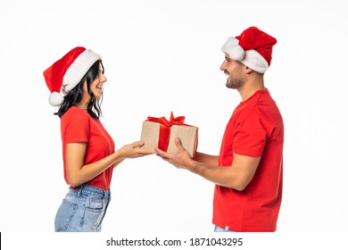 Excited happy couple with gift smiling looking to each other, wear red new year hat cap, isolated over white background - Powered by Shutterstock