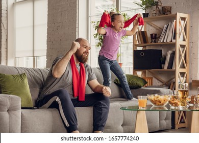 Excited, happy daughter and father watching football, soccer, basketball, tennis, hockey match on the couch at home. Fans emotional cheering for favourite national team. Sport, TV, championship. - Powered by Shutterstock