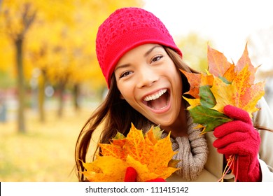 Excited Happy Fall Woman Smiling Joyful And Blissful Holding Autumn Leaves Outside In Colorful Fall Forest. Beautiful Energetic Mixed Race Caucasian / Asian Chinese Young Woman.