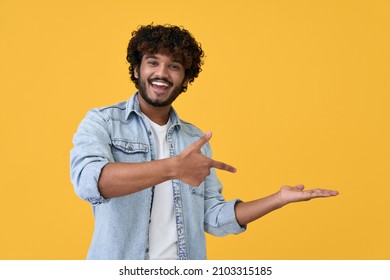 Excited happy positive young indian man student pointing aside with fingers hand gesture at copy space advertising product, presenting sale discount promo offer standing isolated on yellow background. - Shutterstock ID 2103315185