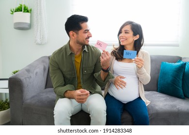 Excited and happy pregnant couple doing a gender reveal of their new baby. Handsome man and beautiful woman looking at each other while holding a pink a blue sign with girl or boy - Shutterstock ID 1914283348