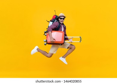 Excited happy young Asian man tourist with luggage jumping isolated on yellow studio background