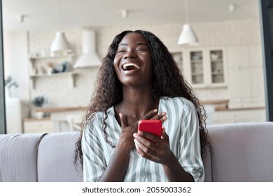 Excited happy young black African woman shopper winner holding cell phone laughing feeling joy getting mobile message in dating app or sms about new job, receiving gift, winning bonus at home. - Shutterstock ID 2055003362