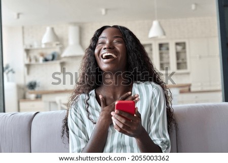 Excited happy young black African woman shopper winner holding cell phone laughing feeling joy getting mobile message in dating app or sms about new job, receiving gift, winning bonus at home.