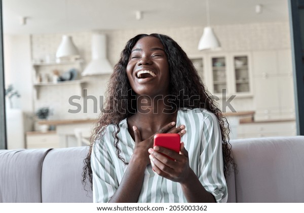 Excited happy young black African woman shopper\
winner holding cell phone laughing feeling joy getting mobile\
message in dating app or sms about new job, receiving gift, winning\
bonus at home.