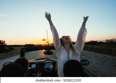 Excited and happy young female traveller or tourist enjoys warmth of summer inside rental convertible or cabriolet car on warm sunny day, palm trees aside road of holiday destination - Powered by Shutterstock