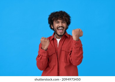 Excited happy young indian man winner looking at camera showing yes gesture feeling happy about betting lottery win, winning prize, getting new job celebrating victory isolated on blue background.