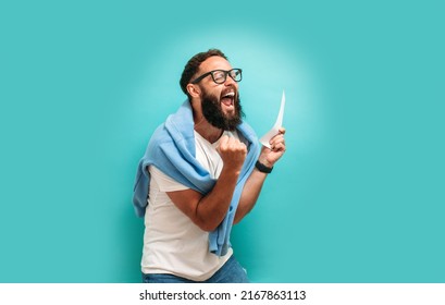 Excited happy young male winner feeling joy winning lottery, placing bets, getting cashback online gift isolated on blue background. Human face emotions and betting concept. Trendy colors - Shutterstock ID 2167863113