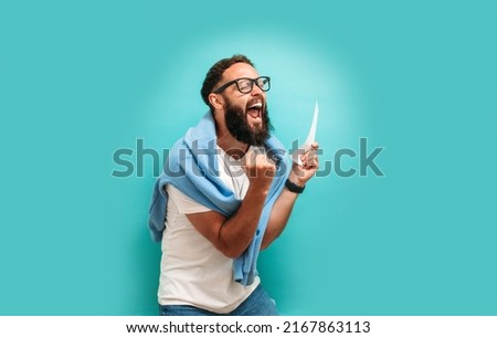 Excited happy young male winner feeling joy winning lottery, placing bets, getting cashback online gift isolated on blue background. Human face emotions and betting concept. Trendy colors