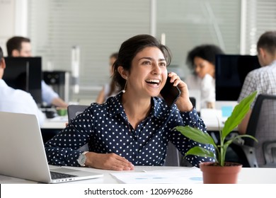 Excited hindu business woman happy to hear good news talking on cell phone in office, smiling emotional indian employee speaking by mobile at work motivated by win success new opportunity promotion