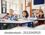 Excited hispanic little girl raising hand in elementary classroom. School children during the lesson trying to answer question in primary school. Cute little latin girl raising hand at school.