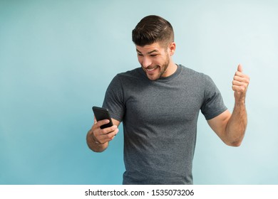 Excited Hispanic Man Reading At Good News On Smartphone Against Turquoise Background