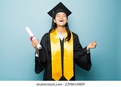 Excited hispanic university graduate celebrating finishing college and receiving her university diploma wearing her graduation gown and celebrating